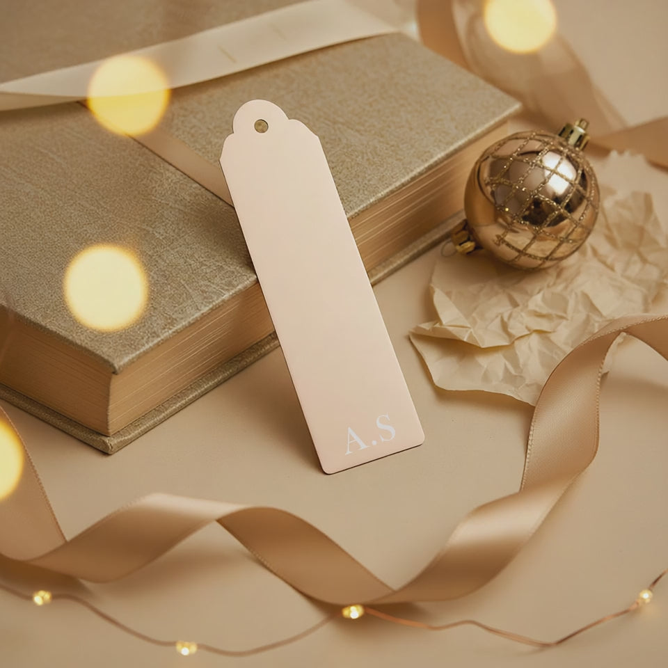 Champagne gold personalised metal bookmark engraved with initials resting on a wrapped book with ribbon and bauble, festive gift for her